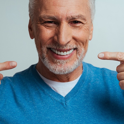 A handsome older man pointing to his white and bright smile.