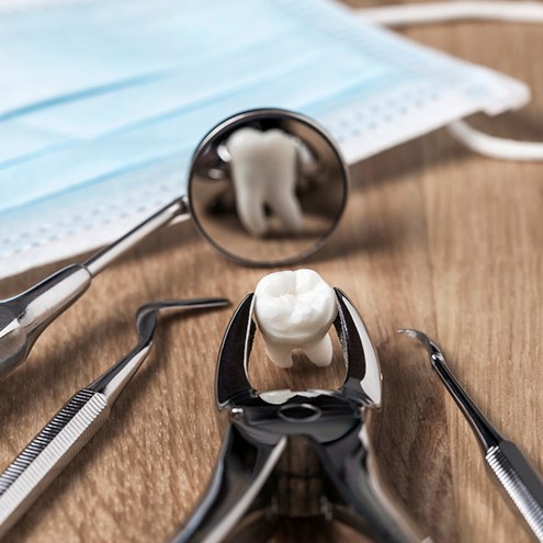 Forceps grasping extracted tooth reflected in dental mirror