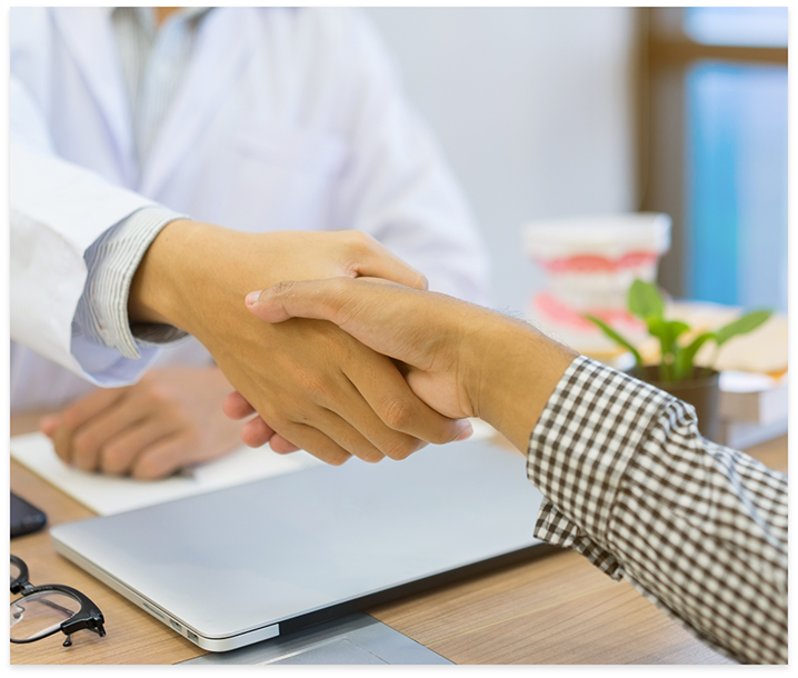 Dentist and patient shaking hands over desk with laptop