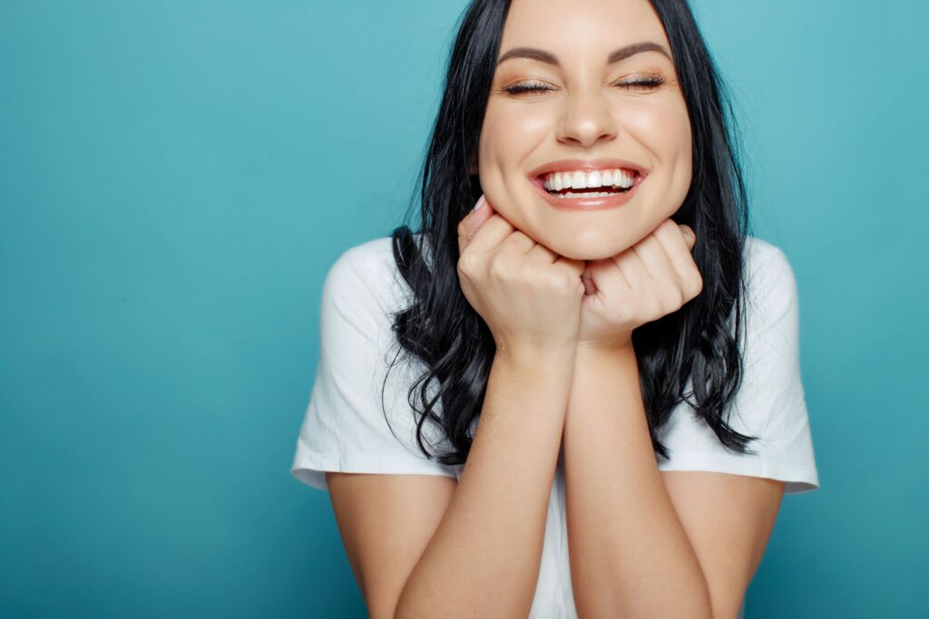 Woman with dark hair resting chin on hands smiling with eyes closed