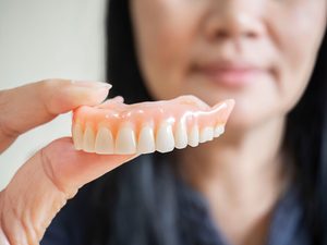 Woman holding upper arch of dentures with thumb and forefinger